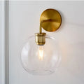 Modern brass wall lamp with clear white glass globe – bedroom